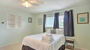 A bedroom with a bed, a nightstand, a ceiling fan, and a window with curtains.