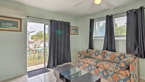 A living room with a sofa, a coffee table, a ceiling fan, and a sliding glass door leading to an outdoor area with a table and chairs.