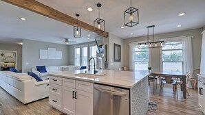 Une cuisine moderne dotée d’un îlot central, de meubles blancs, d’appareils électroménagers en acier inoxydable et de luminaires suspendus.