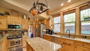 A kitchen with wooden cabinets, stainless steel appliances, granite countertops, and a hanging pot rack. - 'moose Lodge' Cabin w/ Entertainment Gazebo! (Baring)