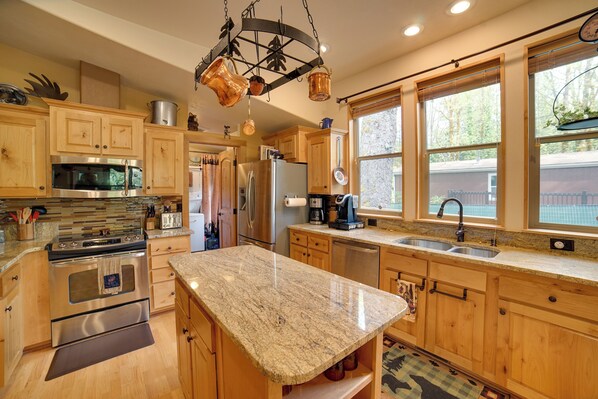 A kitchen with wooden cabinets, stainless steel appliances, granite countertops, and a hanging pot rack.