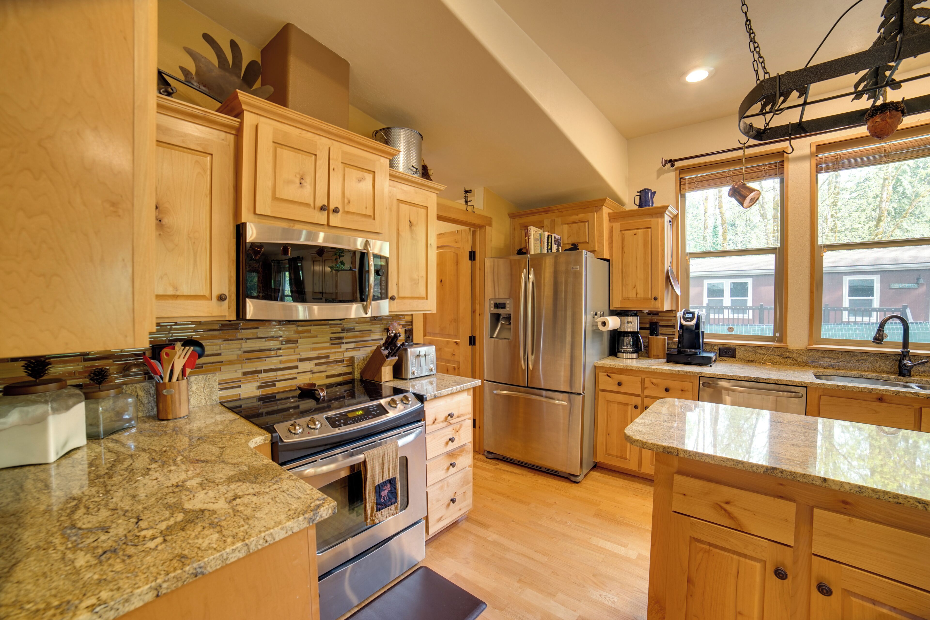 A kitchen with wooden cabinets, stainless steel appliances, granite countertops, and a large window.