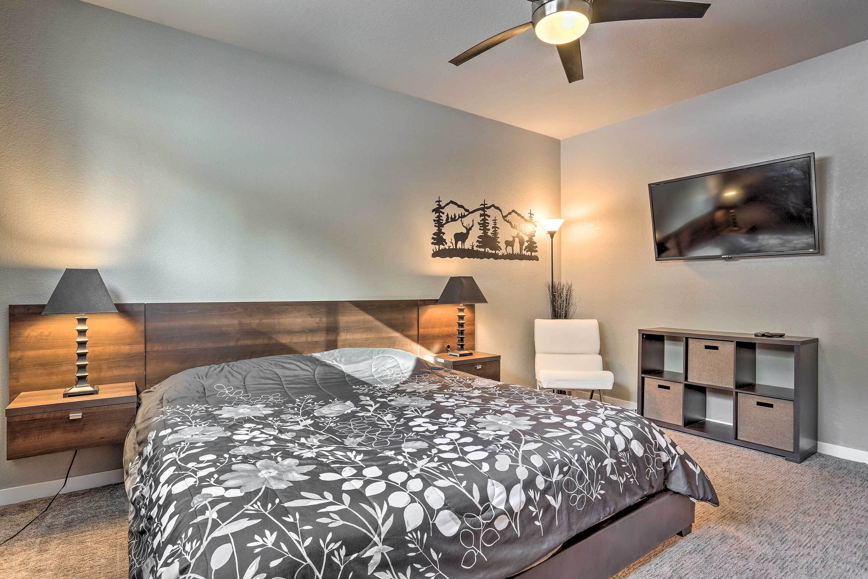 Une chambre à coucher comprenant un lit, des tables de chevet, un téléviseur, un ventilateur de plafond et une étagère fixée au mur.
