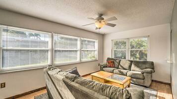 A living room with a ceiling fan, two sofas, a coffee table, and large windows with blinds.