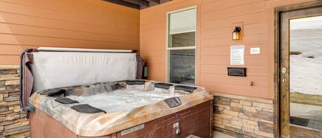A hot tub with a stone wall backdrop, a wooden bench, and a door leading to a snowy landscape.