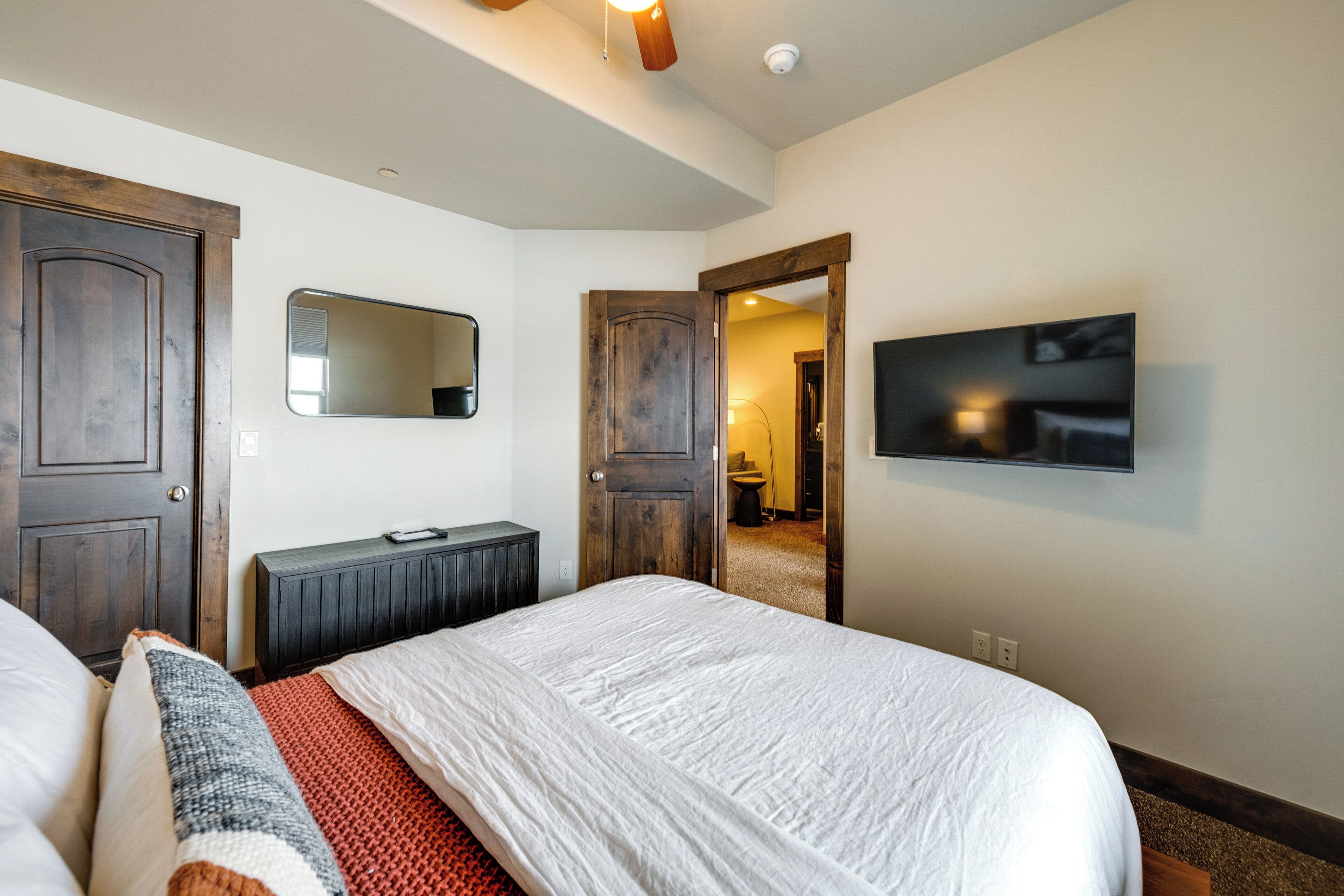 A bedroom with a large bed, a dresser, a mirror, and a television on the wall.