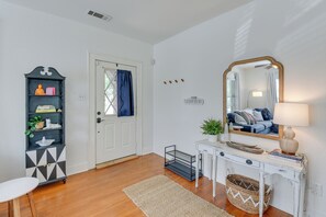 Une pièce avec une porte blanche, un meuble noir et blanc, une console blanche avec un miroir, une lampe et un panier en osier.