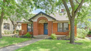 A two-story brick house with a front porch, a blue door, and a small front yard with grass and trees.