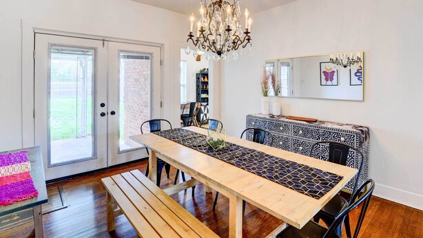 A dining area with a wooden table, benches, and a chandelier. There are chairs around the table, and a patterned table runner.