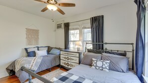 A bedroom with two beds, a ceiling fan, a bedside table with a lamp, and a macrame wall hanging.