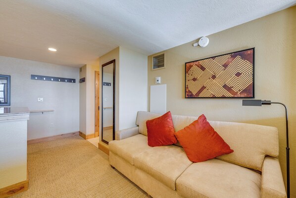 A modern living room with a beige sofa, two red cushions, a large mirror, and a geometric artwork on the wall.