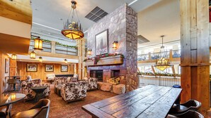 A spacious lobby with a wooden table, chairs, a fireplace, and a high ceiling with skylights. - Ski-in/ski-out Park City Condo: Fireplace & View! (Park City)