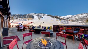 An outdoor seating area with a fire pit, red chairs, and tables overlooking a snowy mountain slope. - Ski-in/ski-out Park City Condo: Fireplace & View! (Park City)
