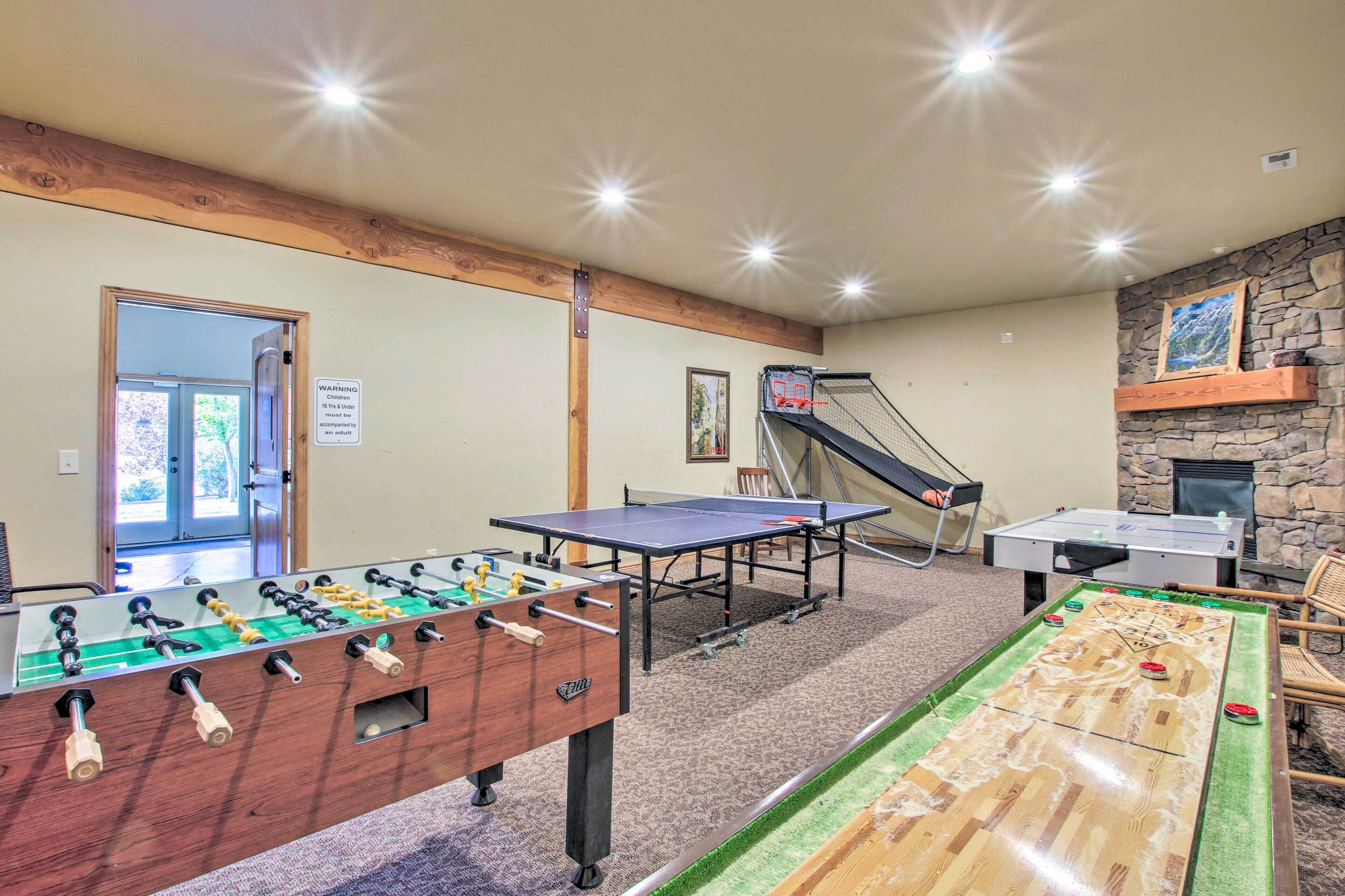 A room with a foosball table, ping pong table, and shuffleboard table.