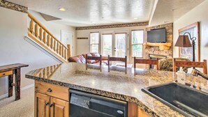 A kitchen with granite countertops, wooden cabinets, a dishwasher, a stone fireplace, and a staircase. - Cozy Eden Condo Retreat < 6 Mi to Ski Resort! (Eden)