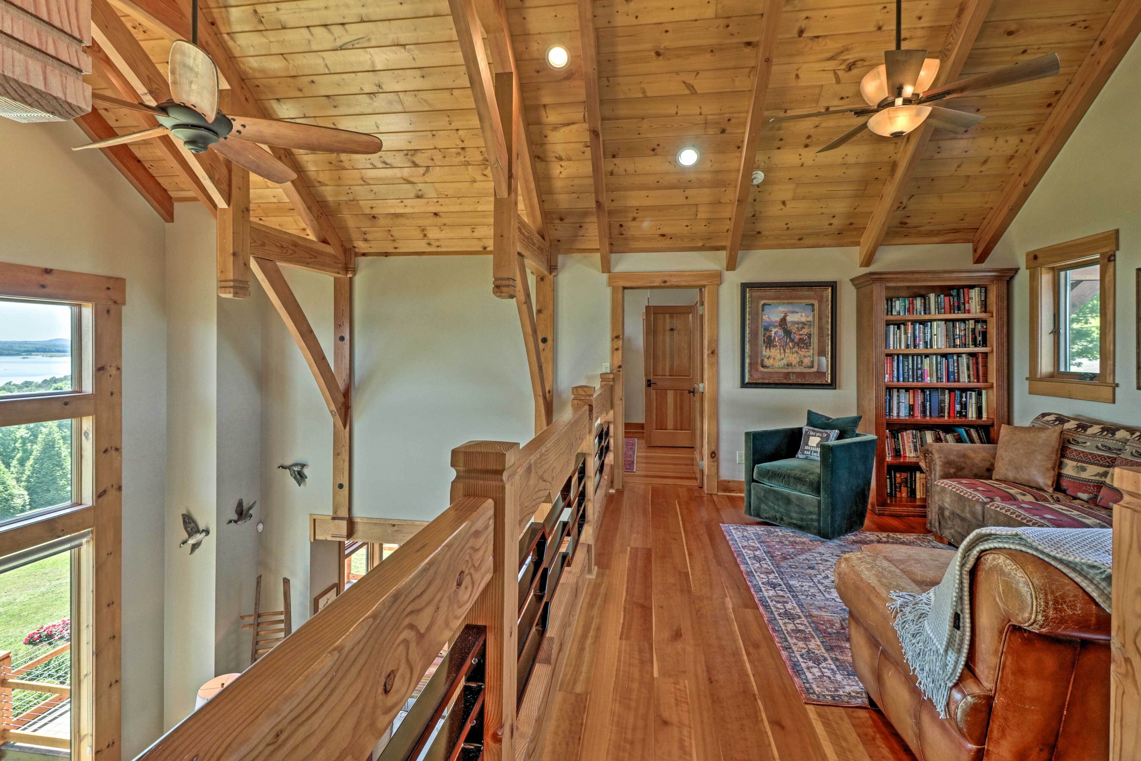A spacious loft-style room with a wooden ceiling, a staircase, a large bookshelf, and a view of the outdoors.