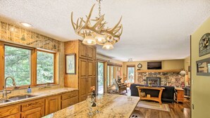 A spacious kitchen with a large island, wooden cabinets, and a unique antler chandelier. - Tranquil Riverside Home w/ Wraparound Deck & Views (Baldwin)