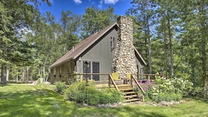 A cabin with a stone chimney, wooden deck, and surrounded by trees. - Tranquil Riverside Home w/ Wraparound Deck & Views (Baldwin)
