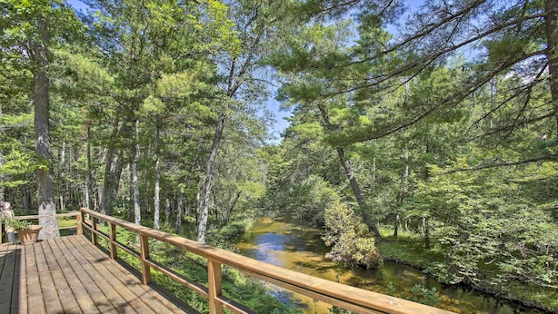 A wooden deck overlooking a forested area with a river. - Tranquil Riverside Home w/ Wraparound Deck & Views (Baldwin)