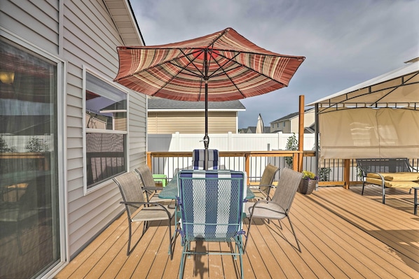 A wooden deck with a table and chairs, a large umbrella, and a view of neighboring houses. - Spacious Family Home w/ Large Deck & Fire Pit! (Caldwell)