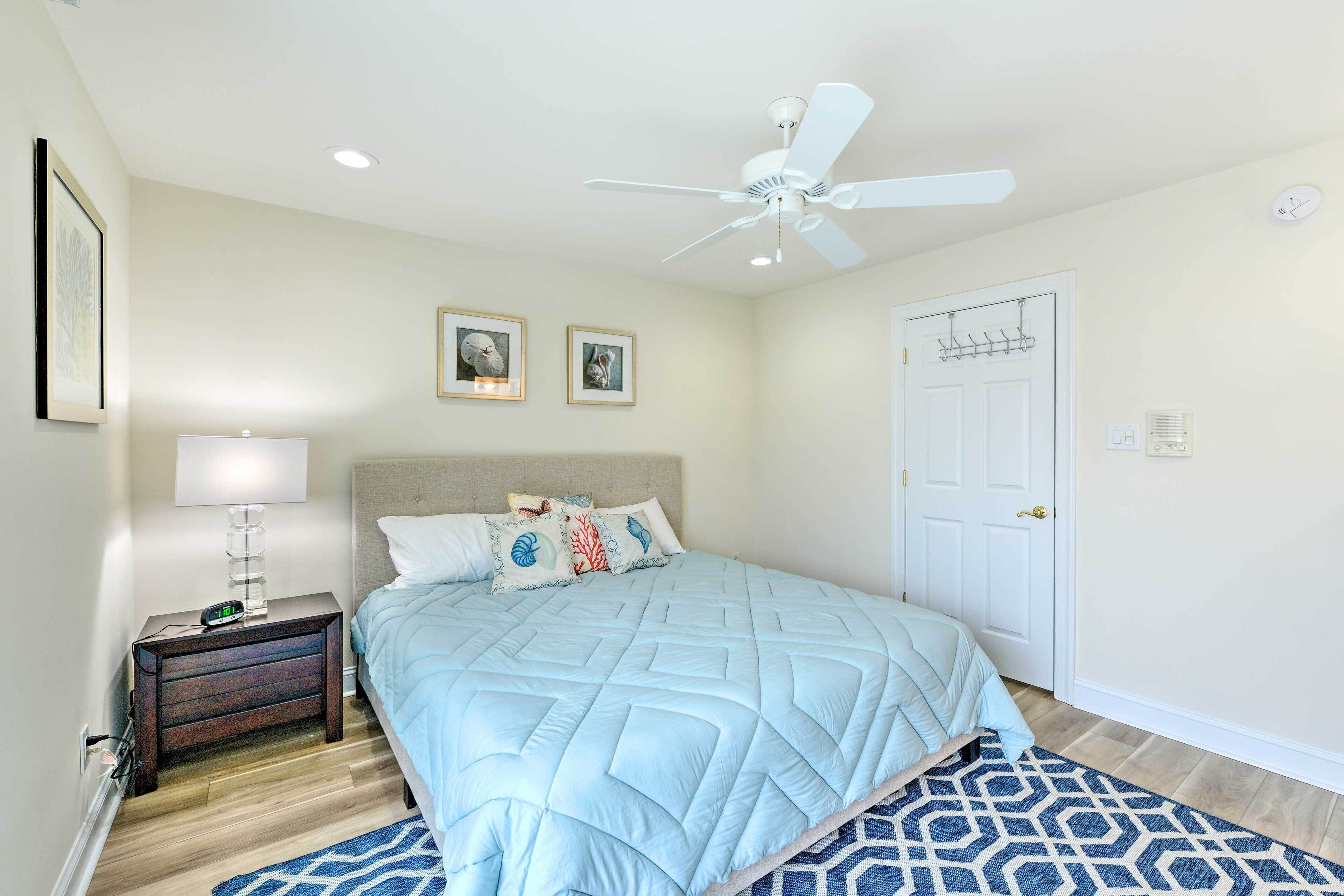 A bedroom with a bed, a nightstand, a ceiling fan, a door, and framed pictures on the wall.