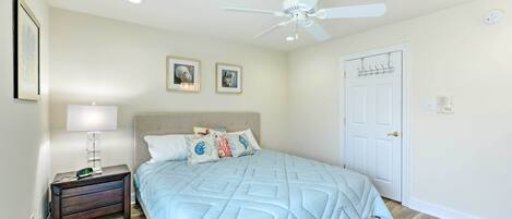 A bedroom with a bed, a nightstand, a ceiling fan, a door, and framed pictures on the wall.