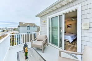 Een balkon met een stoel, een champagnefles en een glas, met uitzicht op een slaapkamer met een bed en een plafondventilator.