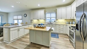 A spacious kitchen with white cabinets, a central island, stainless steel appliances, and a large window providing natural light. - Sunny Brigantine Townhome: Walk to Beach (Brigantine)