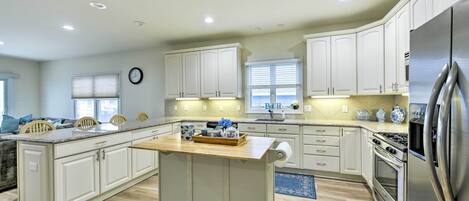 A spacious kitchen with white cabinets, a central island, stainless steel appliances, and a large window providing natural light.