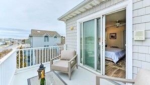 A balcony with a chair, a bottle of champagne, and a glass, overlooking a bedroom with a bed and a ceiling fan. - Sunny Brigantine Townhome: Walk to Beach (Brigantine)