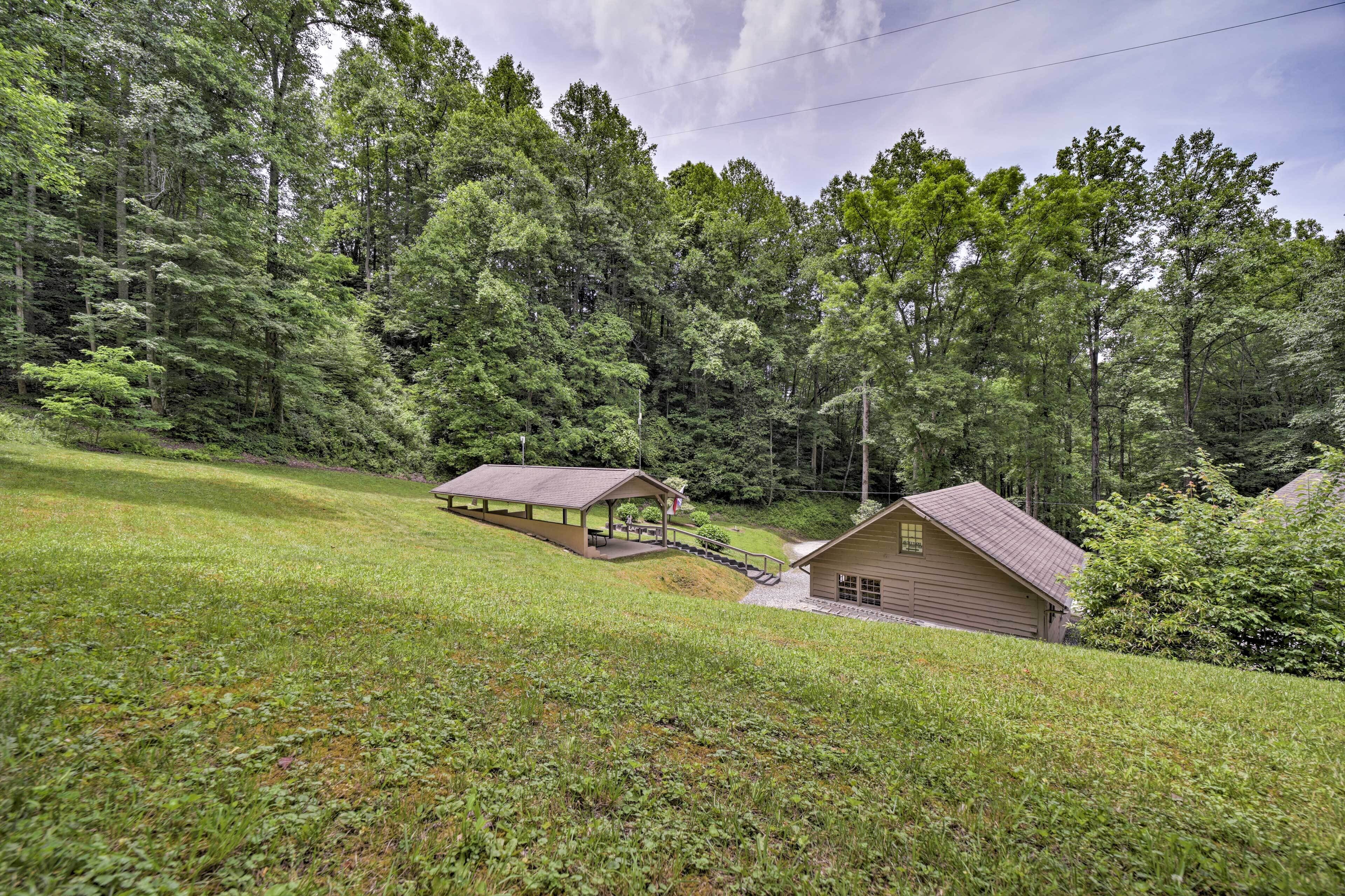 A cabin with a covered porch and a separate building with a sloped roof, surrounded by dense forest.