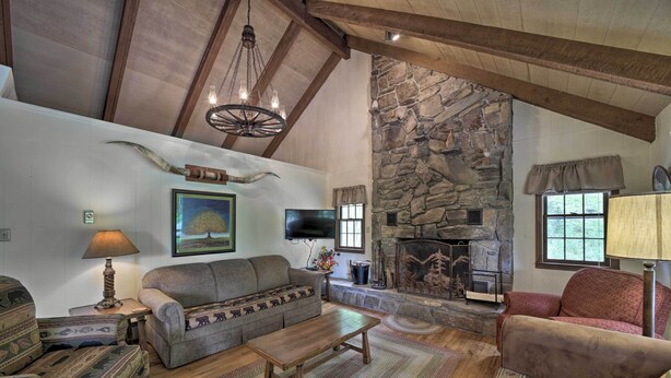 A rustic living room with a stone fireplace, wooden beams, a sofa, and a coffee table. - Mountain Escape w/ Hiking ~ 5 Mi to Bryson City! (Bryson City)