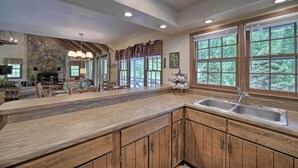 A spacious kitchen with wooden cabinets, a stone fireplace, and large windows offering a view of the outdoors. - Mountain Escape w/ Hiking ~ 5 Mi to Bryson City! (Bryson City)