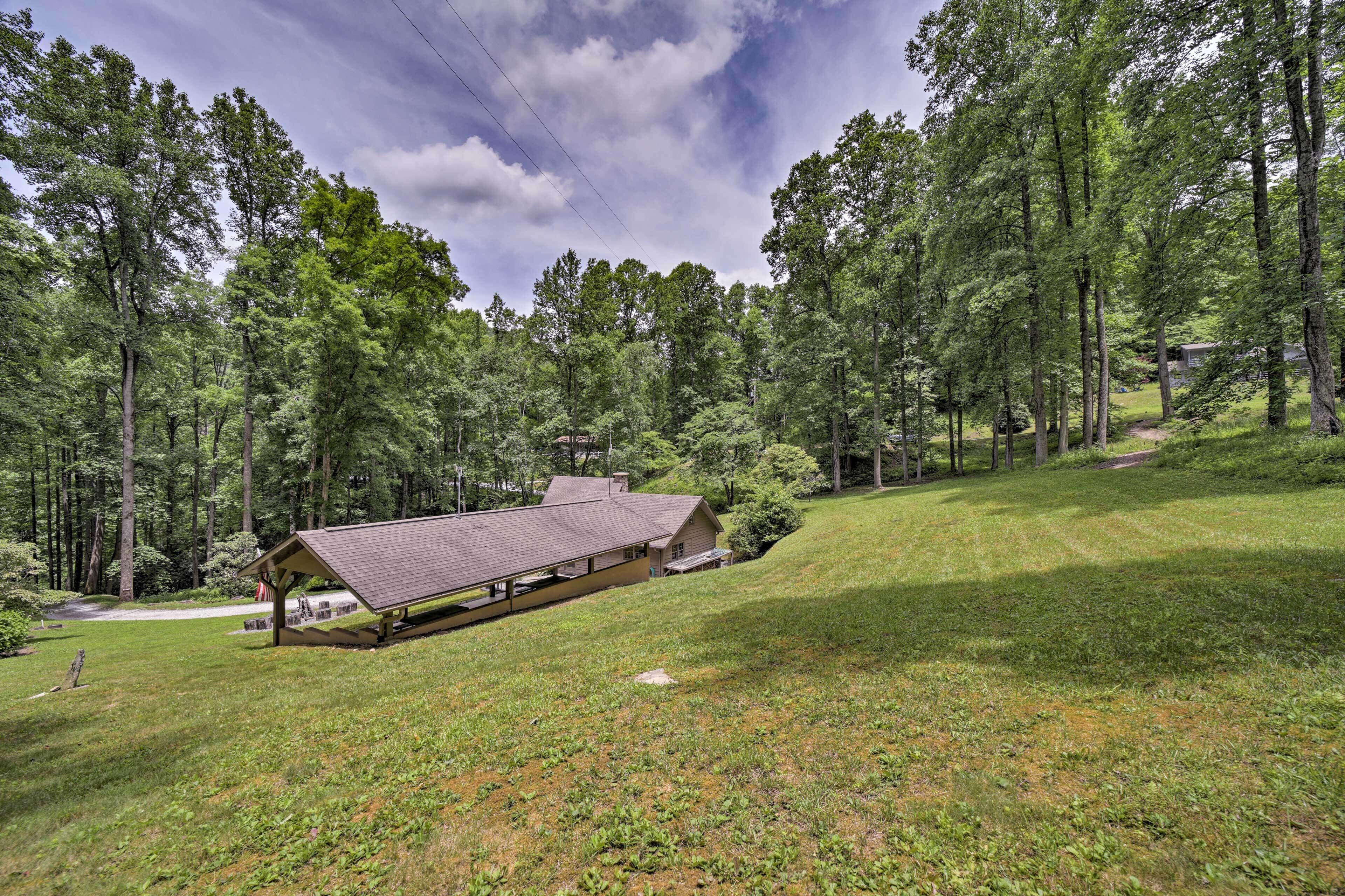 A cabin with a sloped roof, surrounded by a forested area and a grassy hill.