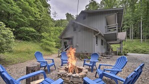 A rustic cabin with a stone fire pit surrounded by blue Adirondack chairs, set in a wooded area. - Mountain Escape w/ Hiking ~ 5 Mi to Bryson City! (Bryson City)