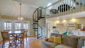 A spacious living area with a dining table and chairs, a sofa with cushions, a staircase to a loft, and a kitchen with white cabinets and appliances. - Resort Living on Lake of the Ozarks! Family Cabin (Osage Beach)