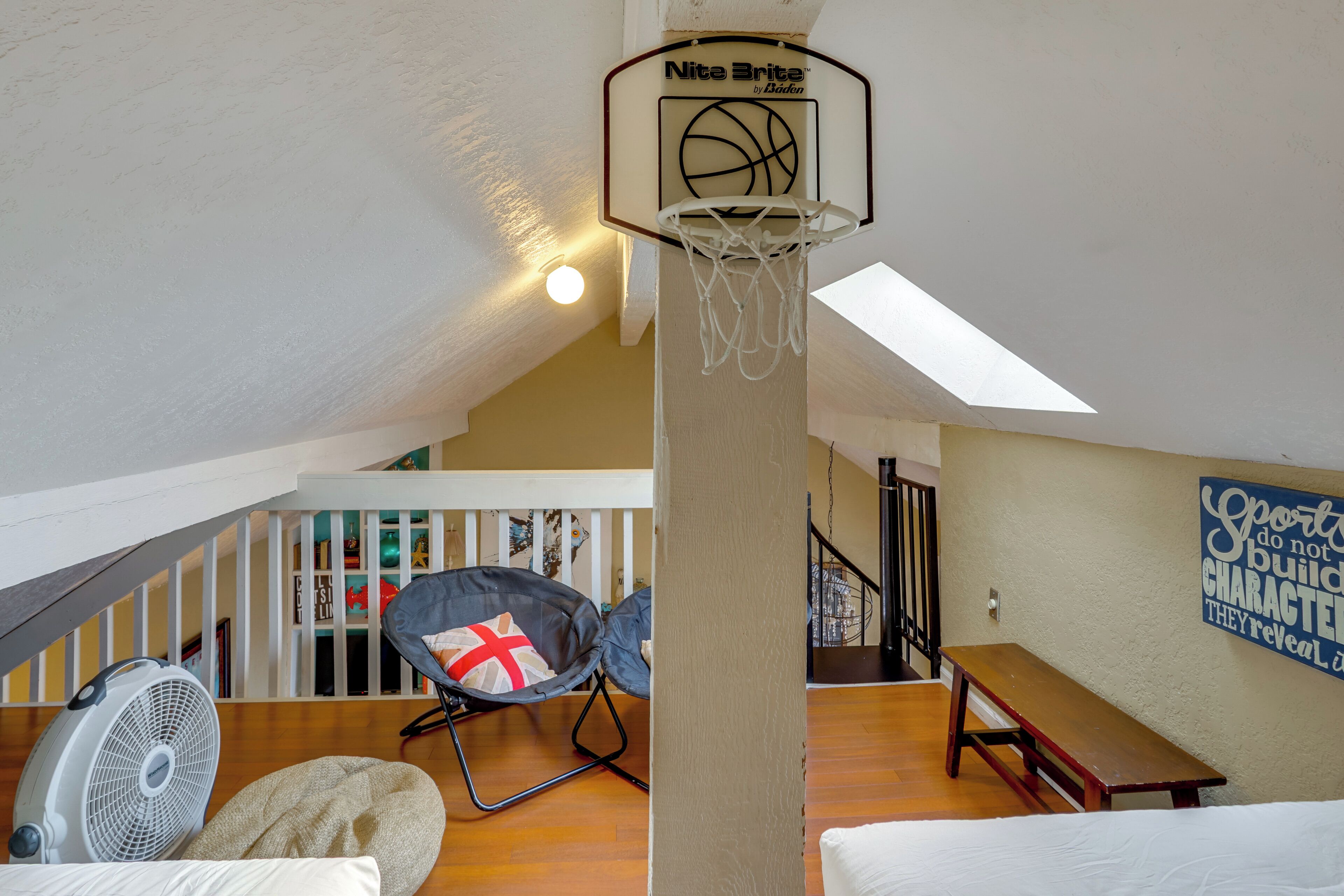 A loft-style room with a basketball hoop, a fan, a bean bag chair, and a wooden bench.
