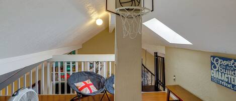 A loft-style room with a basketball hoop, a fan, a bean bag chair, and a wooden bench.