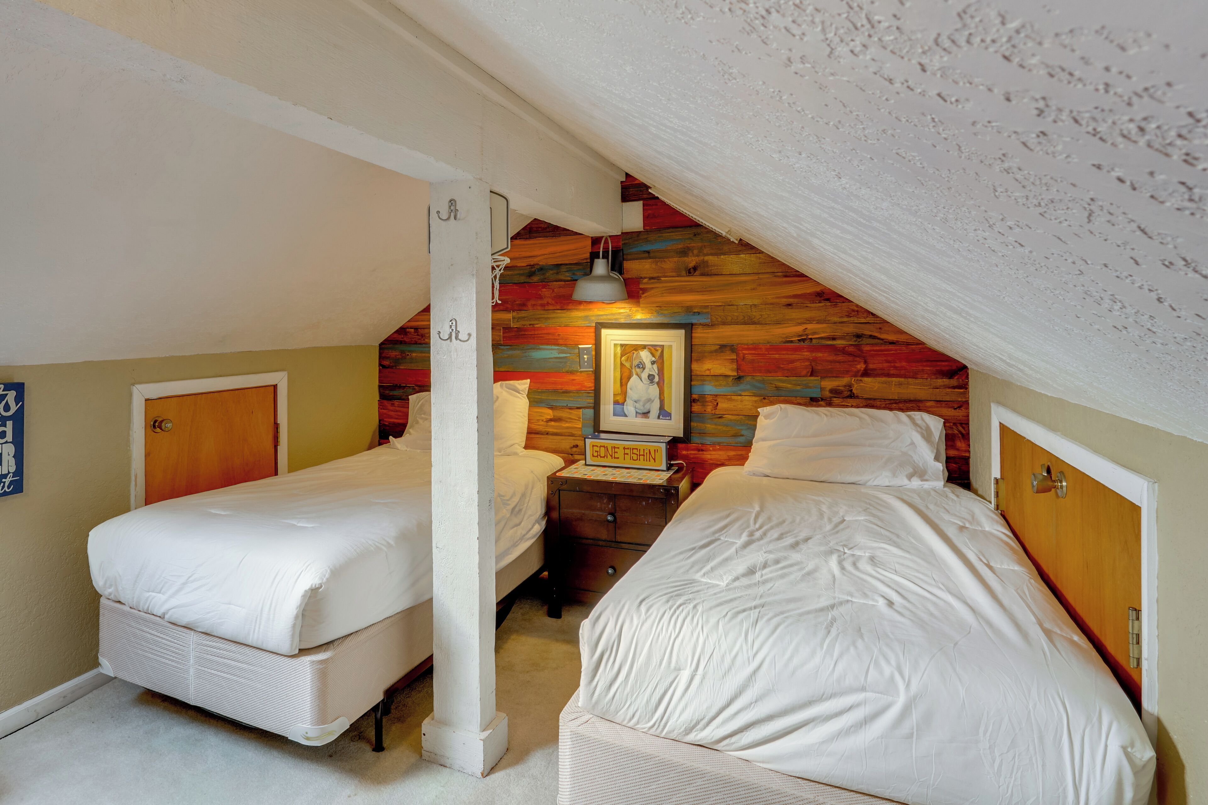Une chambre avec deux lits, un plafond en pente en bois et un tableau encadré au mur.