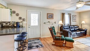 A modern kitchen with a bar stool area, a living room with a leather sofa and a rocking chair, and a ceiling fan. - Pierre Vacation Rental w/ Grill & Fenced Yard (Pierre)