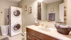A laundry area with stacked washers and dryers, a sink with toiletries, and a mirror reflecting a towel rack. - Pierre Vacation Rental w/ Grill & Fenced Yard (Pierre)