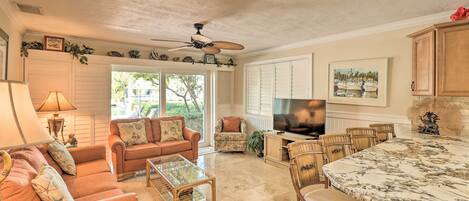 A spacious living room with a large TV, comfortable seating, and a dining area with a marble table.