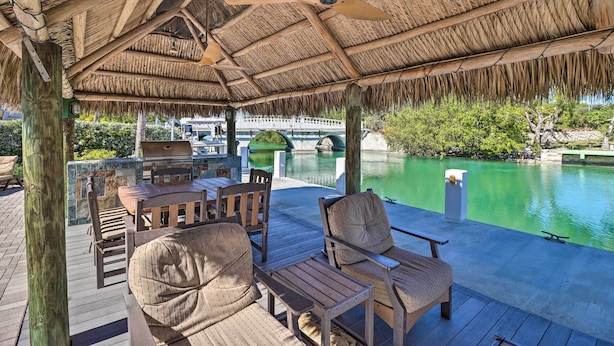 An outdoor patio with wooden furniture and a thatched roof, overlooking a pool. - Marathon Vacation Rental With Pool Access! (Marathon)
