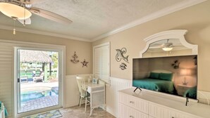 A room with a sliding glass door leading to a pool, a white dresser, a television, and decorative wall art. - Marathon Vacation Rental With Pool Access! (Marathon)