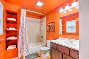A bathroom with an orange wall, a white bathtub, a toilet, a sink, and a shower.