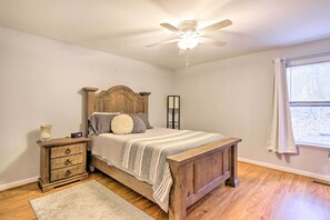A bedroom with a wooden bed, a nightstand, a bedside table, a ceiling fan, and a window with curtains.