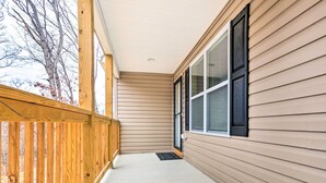 Un porche abrité avec une balustrade en bois, un revêtement de couleur beige et une porte noire.