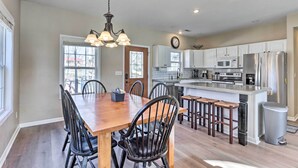A modern kitchen with white cabinets, stainless steel appliances, and a wooden dining table with chairs. - Lakefront Camdenton Home w/ Fire Pit & Grill! (Camdenton)