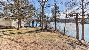 A lakeside property with a house, trees, and a clear view of the water. - Lakefront Camdenton Home w/ Fire Pit & Grill! (Camdenton)