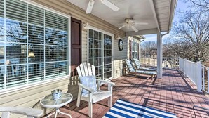 A covered porch with a ceiling fan, a white Adirondack chair, a small table, and a blue and white striped rug. - Lakefront Camdenton Home w/ Fire Pit & Grill! (Camdenton)